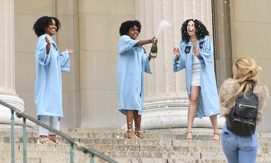 Three grads pop champagne on Low Steps while a photographer walks by. 