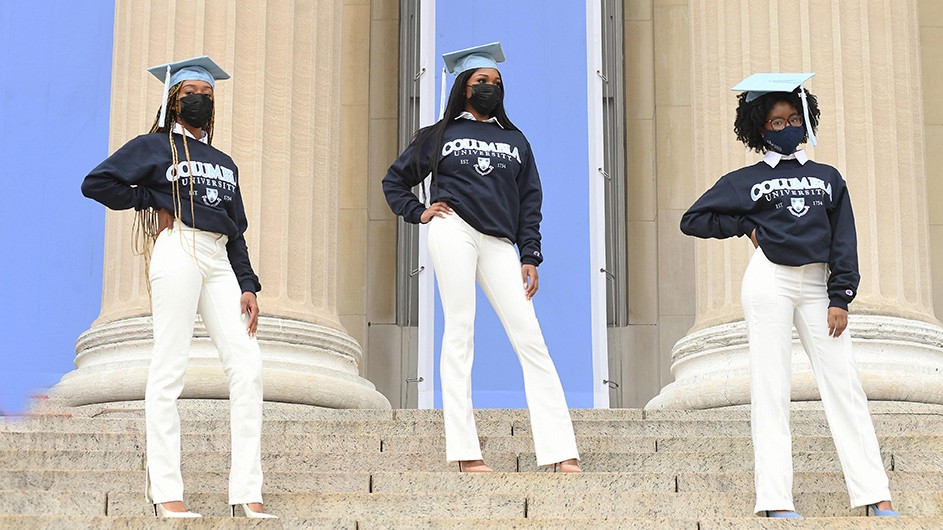 Three women in Columbia sweatshirts and mortarboards pose on Low Steps.