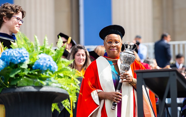 Mabel Wilson holds to the ceremonial mace in a red gown and black hat. 