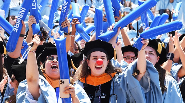 A nursing graduate with a red clown nose cheers with the rest of her graduating class. 