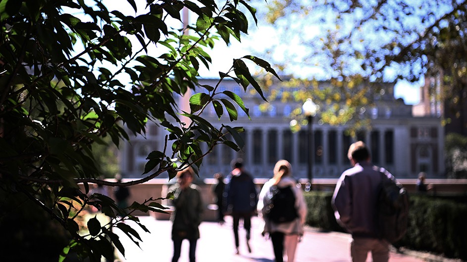 Students, faculty, and staff walking around the Columbia Morningside campus with Butler Library in the background. 
