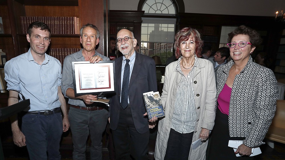 Five people posing for a photo with a book and a certificate