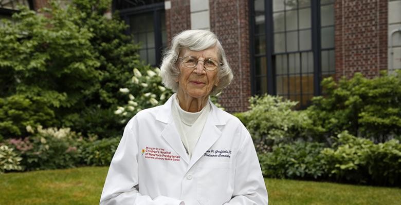 Dr. Sylvia Preston in a white lab coat stands outdoors in front of a green lawn