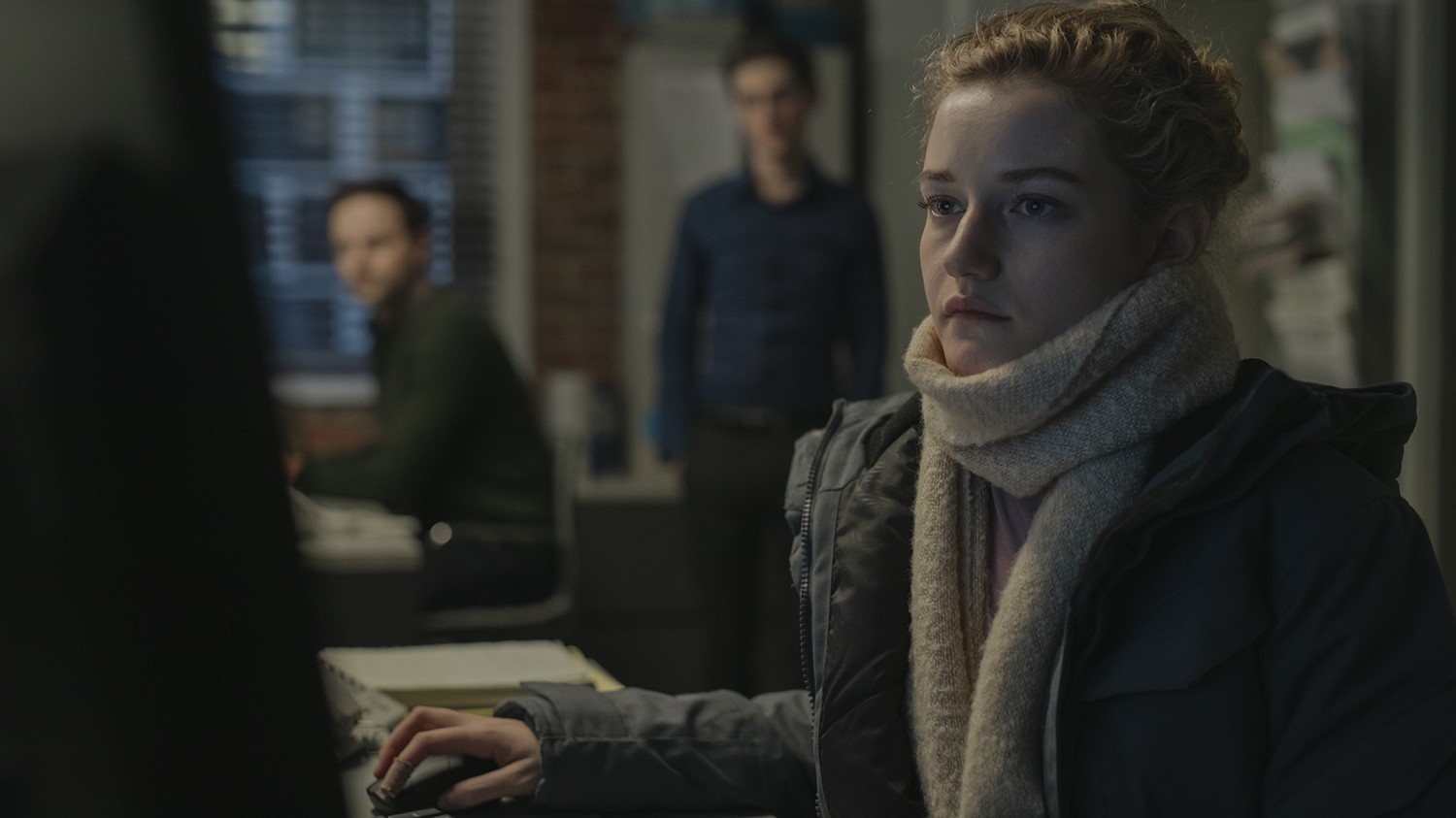 A woman wearing a white scarf sits in front of a computer with two men looking on.