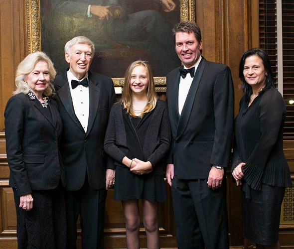 Five people dressed in black formal wear standing and posing in front of a picture