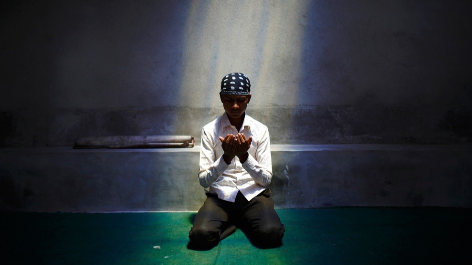 A muslim boy kneeling down and praying under a spotlight