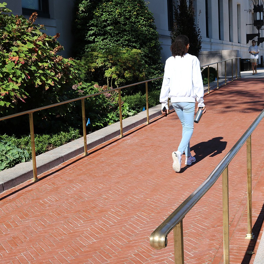 A young woman walks up a masonry ramp with bronze rails that leads up to the Butler Library North entrance.