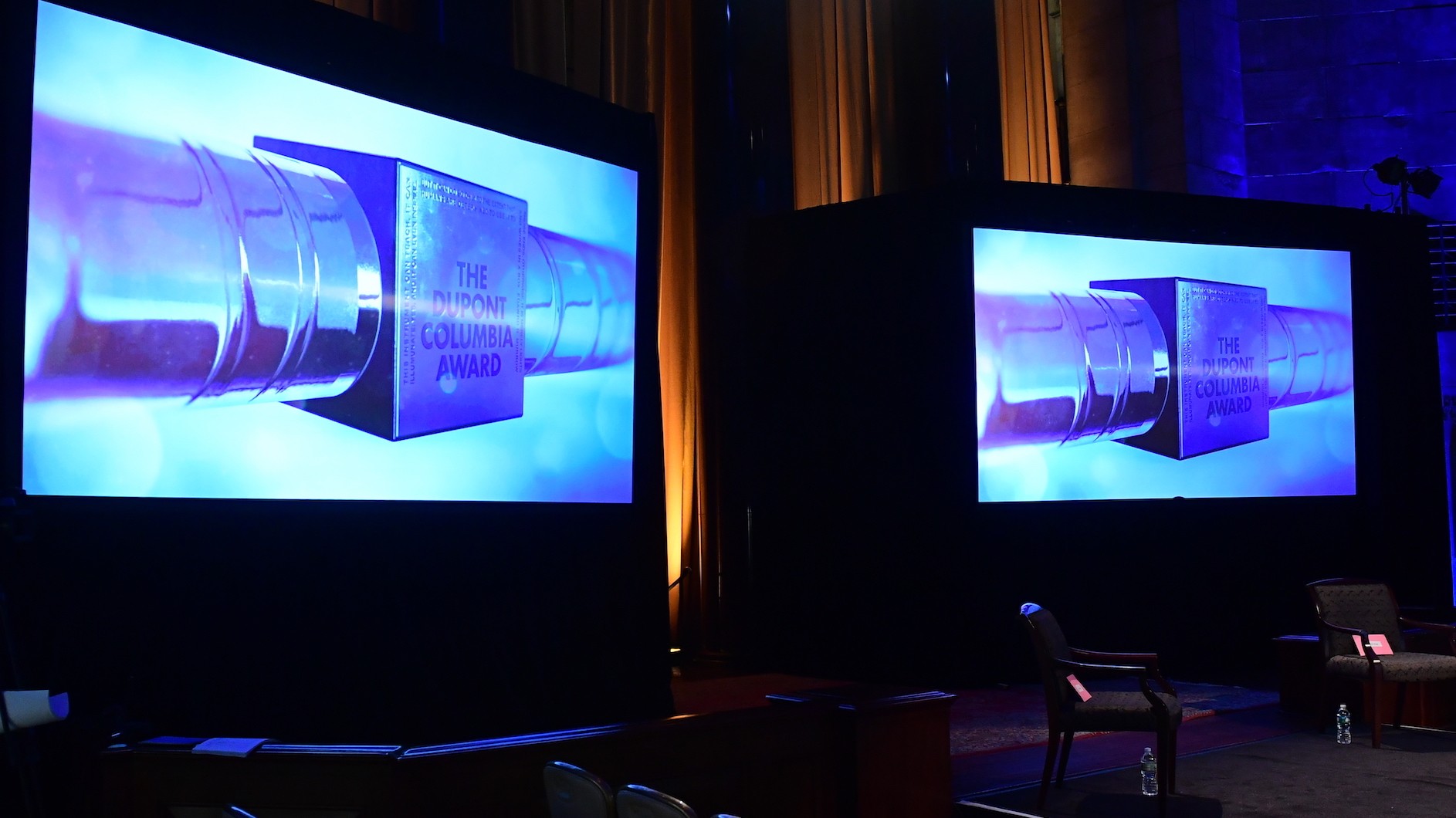Two big screens with identical images of a silver baton with duPont Columbia Award written on them