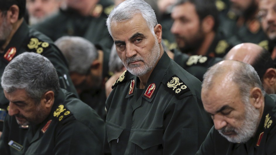 Iranian General Qasem Soleimani with gray hair and dressed in green military uniform surrounded by other Iranian officers in similar uniforms.