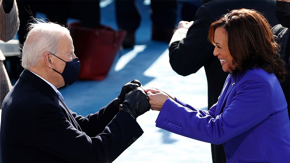Joe Biden, in a black coat, double fist-bumps Kamala Harris, in a purple coat, on inauguration day 2021.