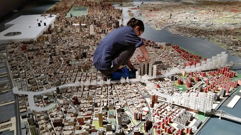 A woman stoops to work on a structurein the middle of a three-dimensional panoramic model of New York City.