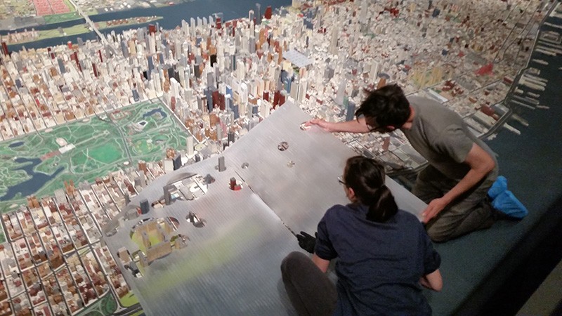 Two people lean over a three-dimensional model of Manhattan