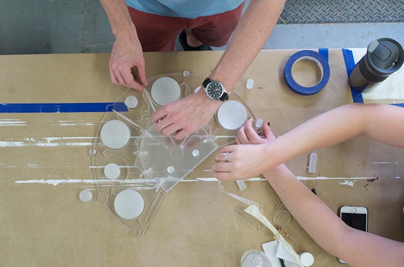 One person holds a clear,plastic mold in place while another fills cavities in the mold with a white liquid.