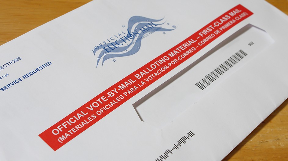 white letter with red stripe and in white letters it says Official Vote by Mail First Class. Black bar code below