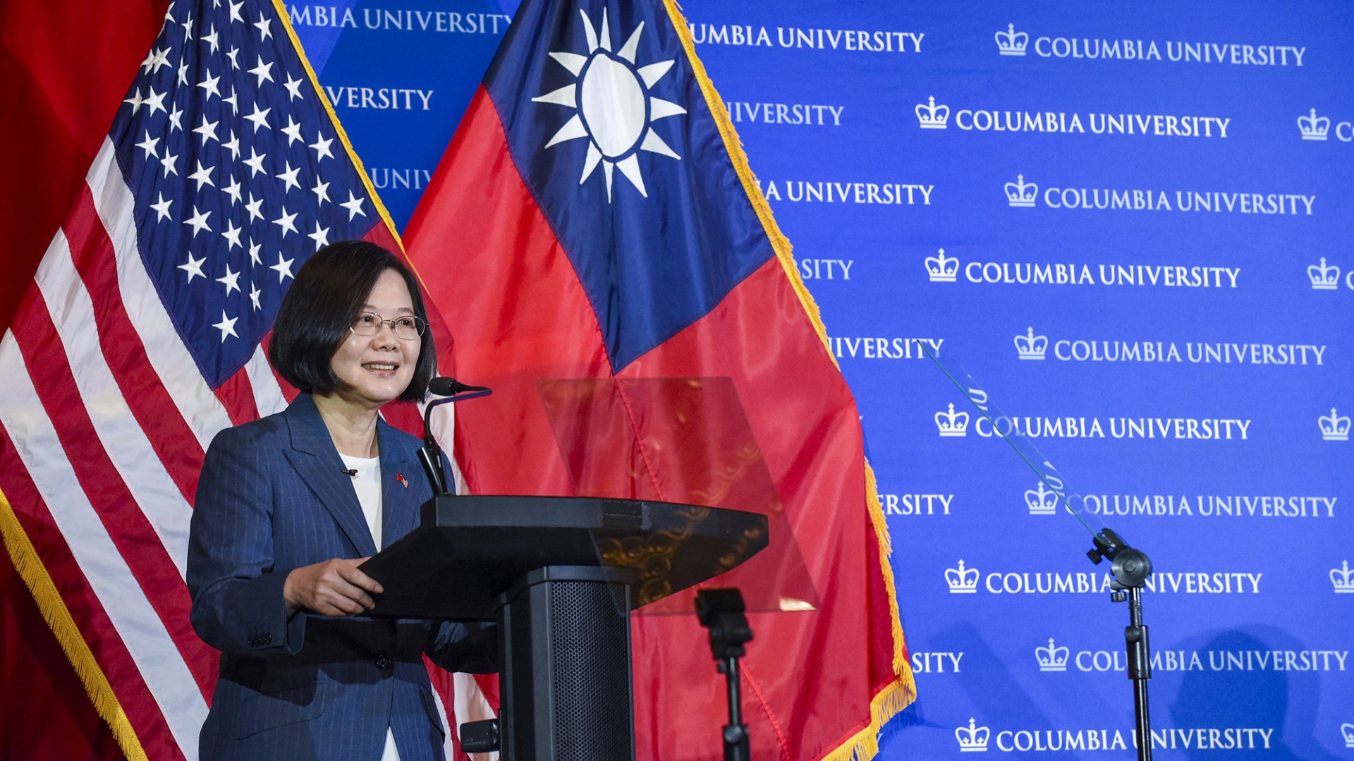 A woman wearing glasses standing in front of American and Taiwanese flags
