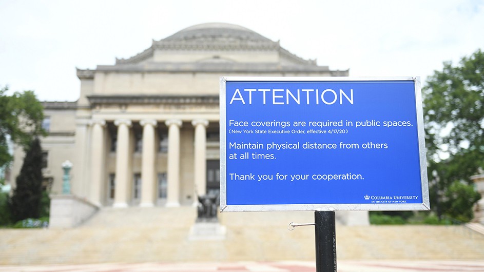 blue sign with white lettering about safety measures in front of beige building with large columns 