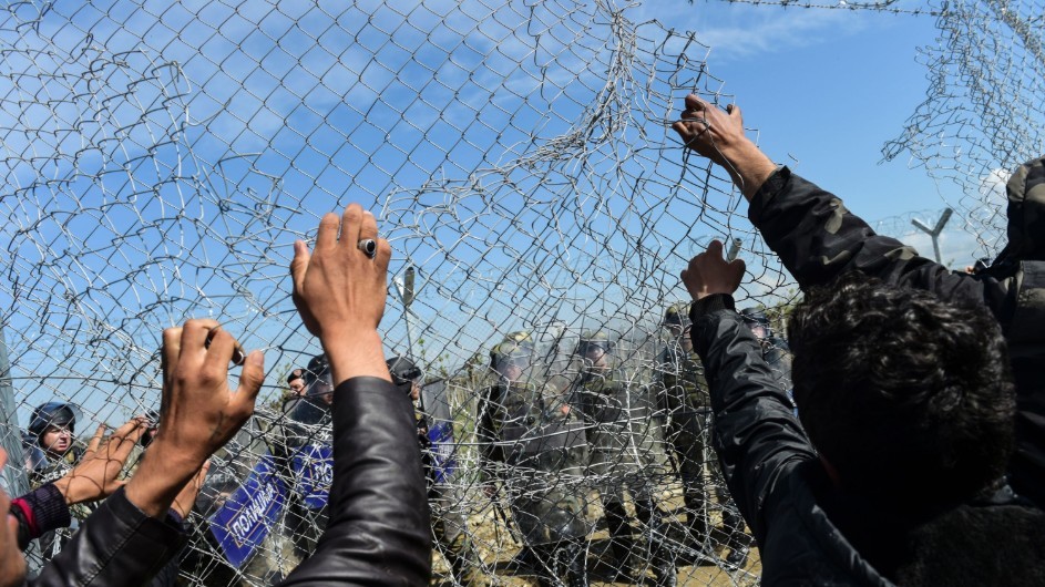 hands grabbing onto torn up wire fences with soldiers standing on the other side