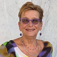 A photo of a woman wearing a colored shirt, jewelry and glasses.