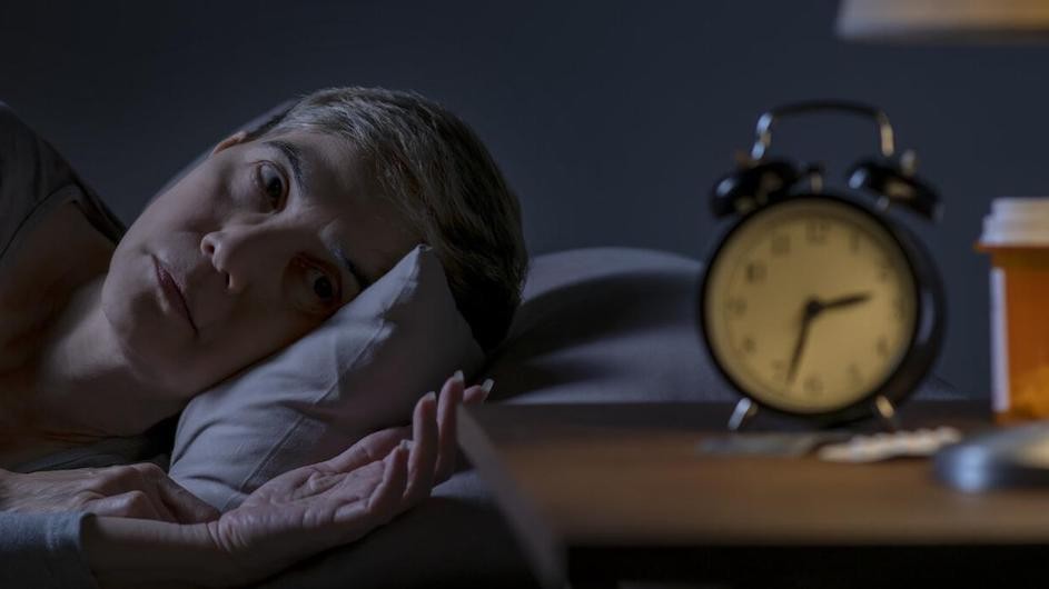 A woman lying awake at night looks at her clock.