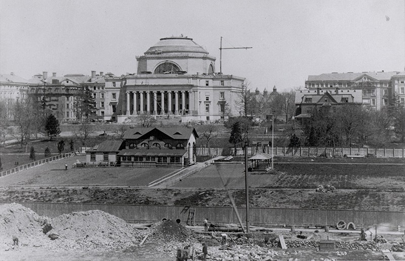 a vintage black and white distant image of low library appearing to be completely constructed.  Area surroudning the Low area is mainly dirt filled and under construction while men are at work on the grounds.