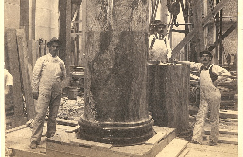 black and white interior image of low library while under construction. men are at work standing near marble columns dressed in overalls and hats.