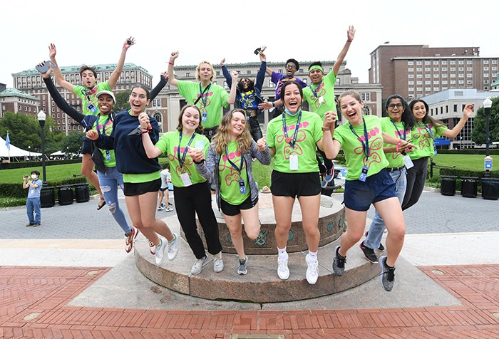 Columbia students in green shirts jump off the sundial. 