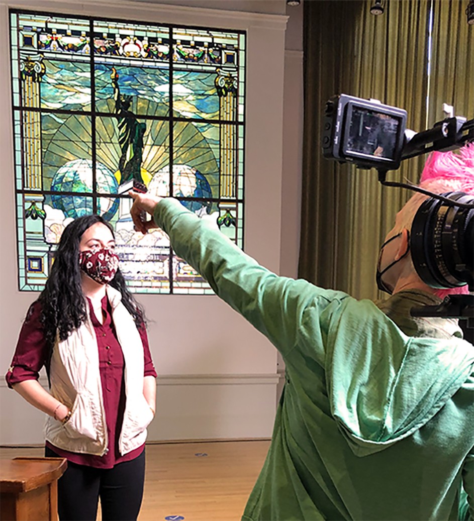A stand-in poses in front of a stained glass window while being filmed.