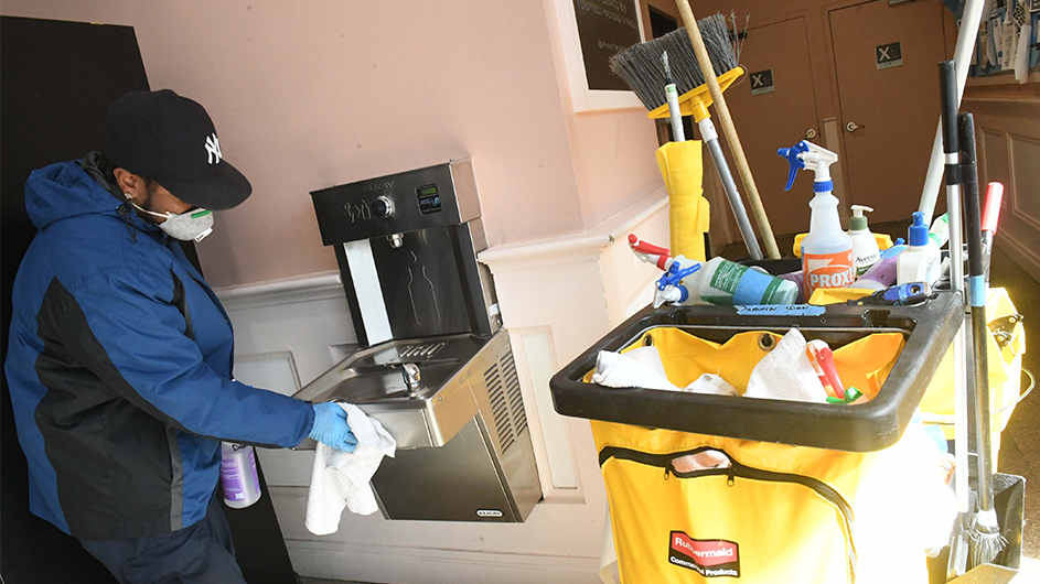 Photo By Eileen Barroso A worker in a coat, hat, and, mask cleans a water bottle filter.