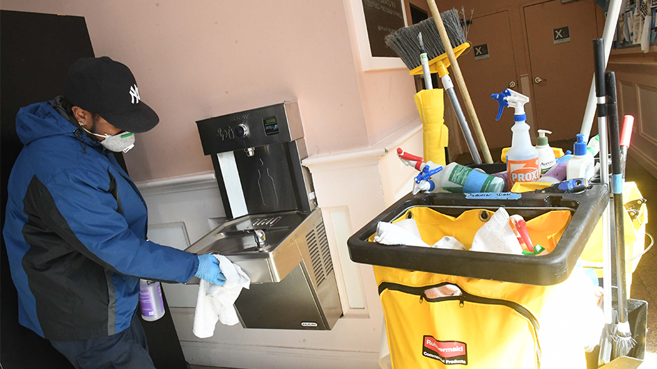 A worker in a coat, hat, and, mask cleans a water bottle filter. 