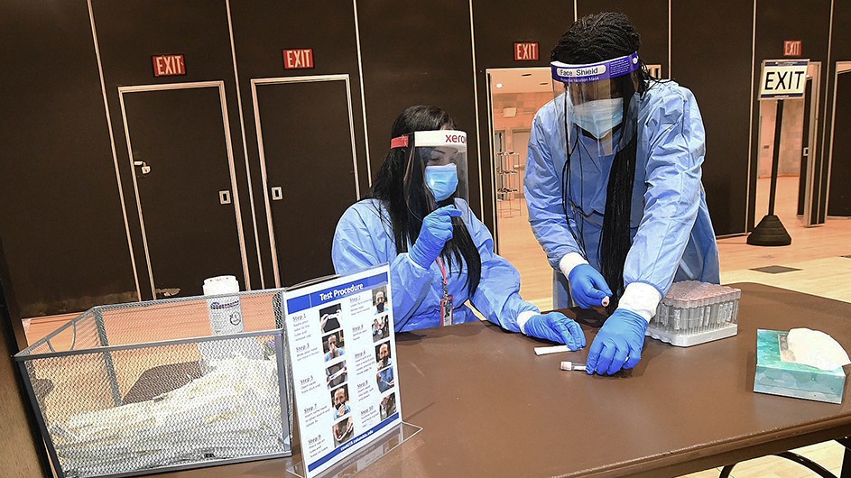 Photo by Eileen Barroso Two essential workers in PPE prepare vials for COVID testing on Columbia's campus.