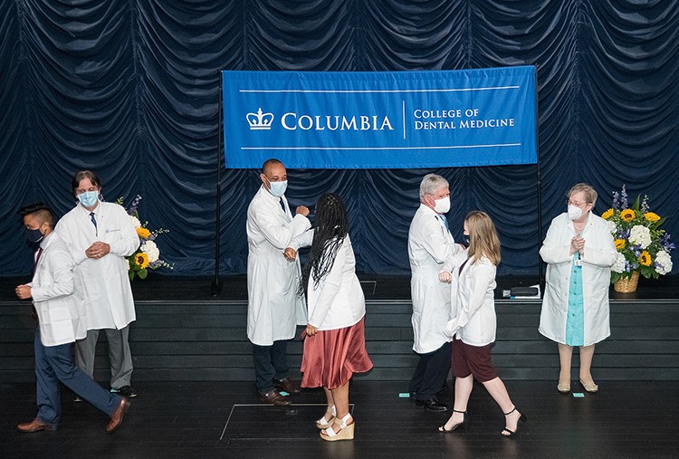 Students in white coats bump elbows with doctors. 
