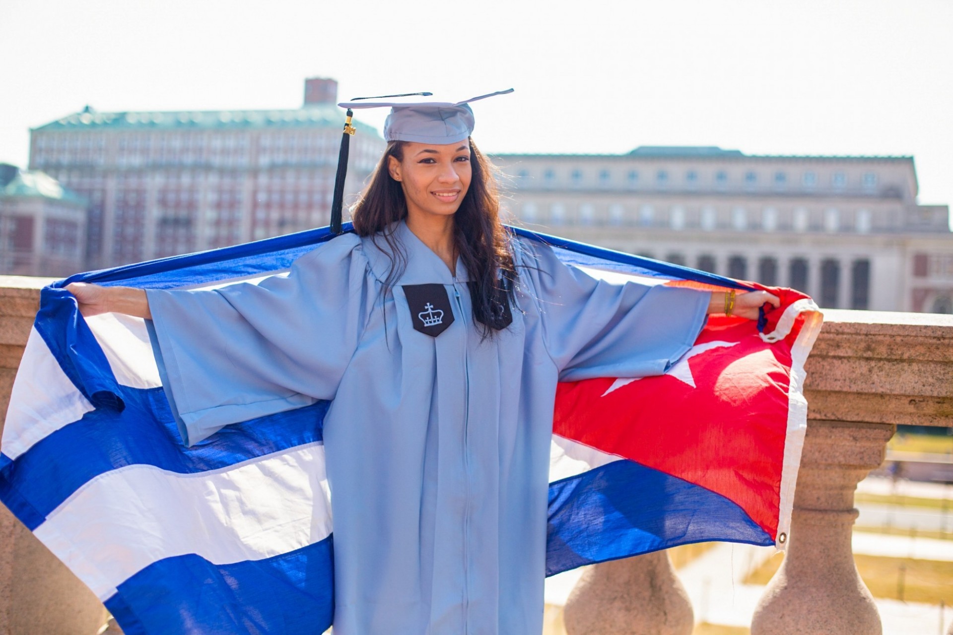 Emily Carrero stands in Columbia regalia with a Cuban flag behind her.