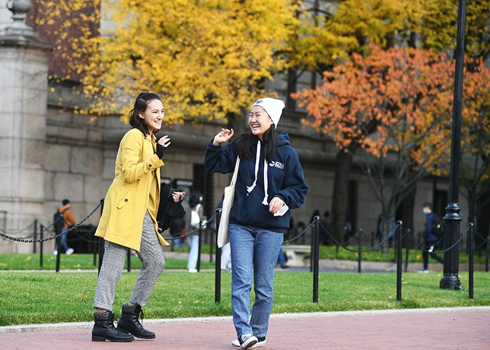 Two friends chat on Columbia's college walk with a yellow tree behind them. 