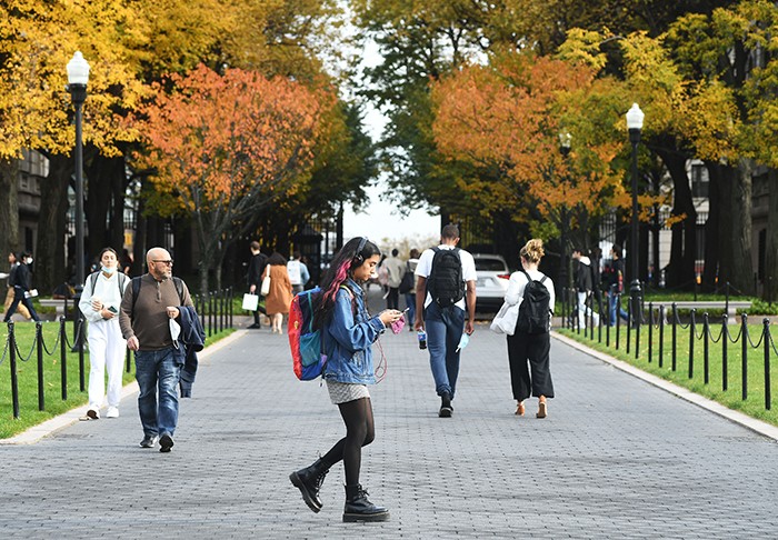 A student in headphones walks with leaves behind her. 