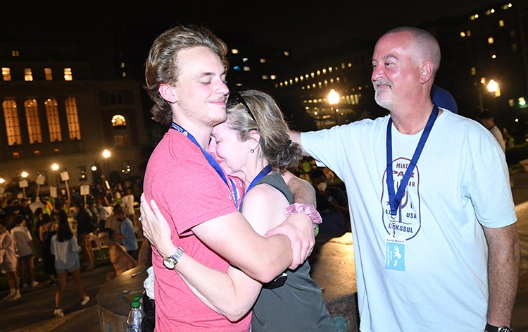 A mom hugs her son in a pink shirt while the father looks on. 