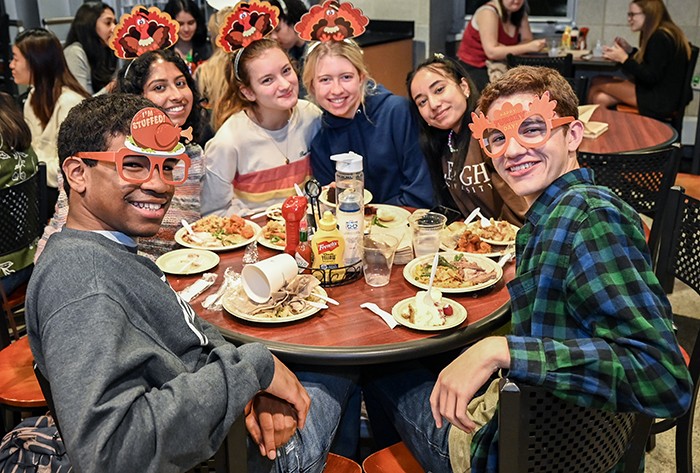 A group of friends in a Dining Hall wear turkey masks. 