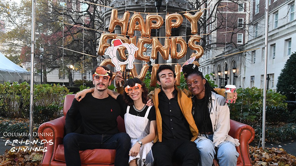 Four friends sit on an orange couch at Van Am Quad at Columbia Dining's Friendsgiving