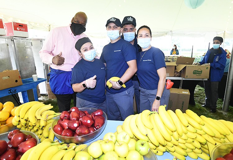 Columbia Dining staffers stand with a table full of bananas and apples. 