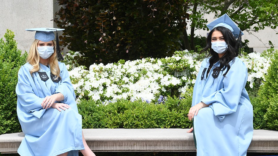 Two Columbia graduates in regalia wearing masks. 