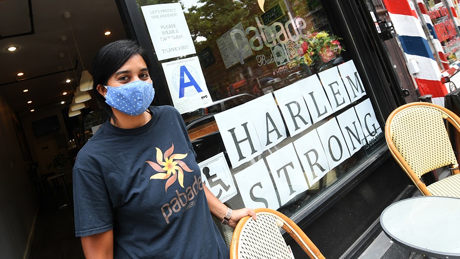 A dining worker in Harlem poses in front of a sign reading "HARLEM STRONG"