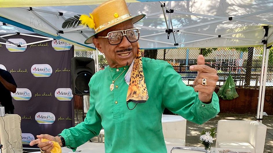 A man in a green suit and golden hat dances. 