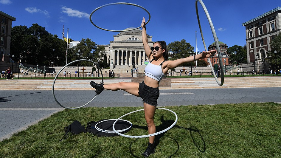 Maia Oceana Castro-Santos (CC'25) spins hula-hoops on Butler Lawn. Photo by Eileen Barroso/Columbia University. Maia Oceana Castro-Santos spins four hula-hoops around her legs and arms on Butler Lawn.