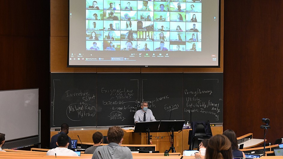 Students sit in a classroom with masks on while other students are on Zoom.