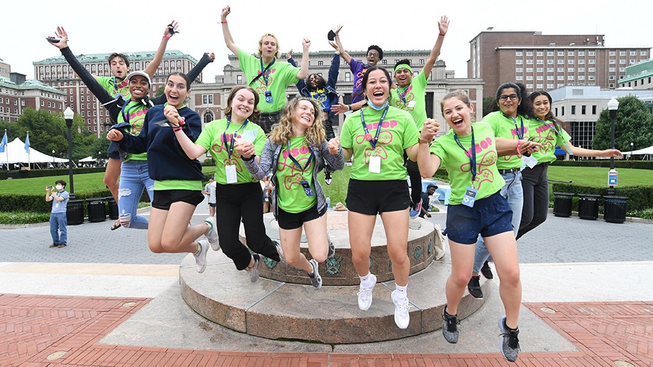 A group of students jump for joy at New Student Orientation Program activities during the week of August 29, 2021. Photo by Eileen Barroso. A group of students in green shirts jump off the sundial in Low Plaza.