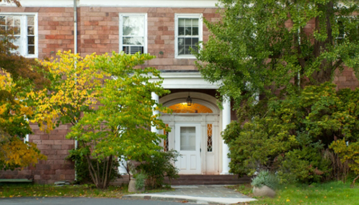 A view of the front of Lamont Hall among the bushes.