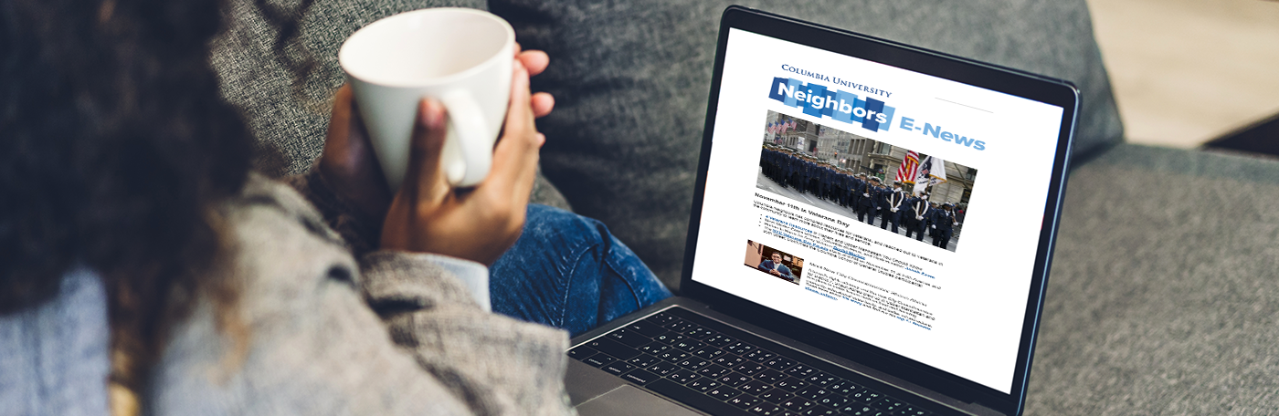 A woman reads the Neighbors enews on her laptop with a cup of coffee