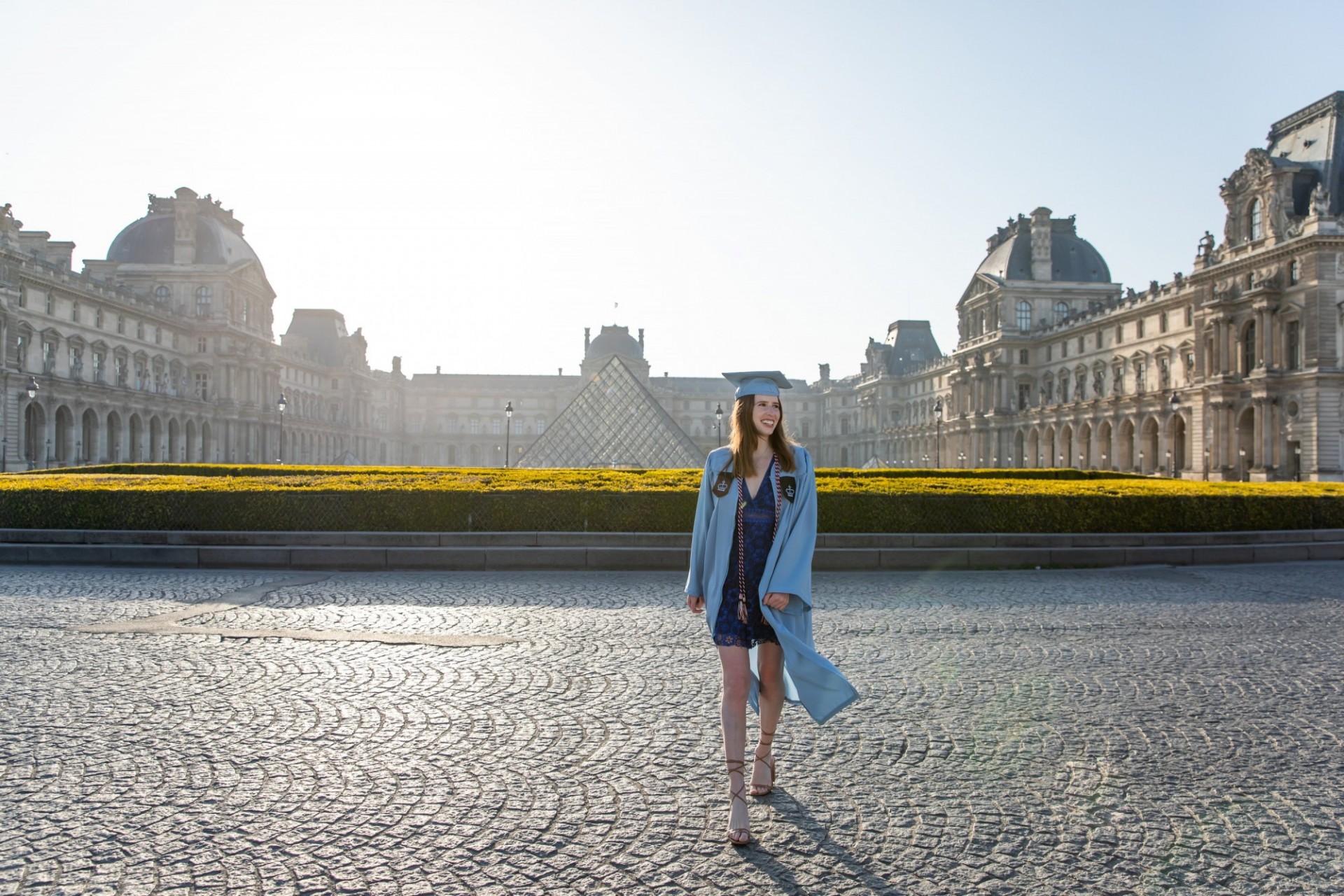 A columbia student in regalia poses in front of the louvre. 