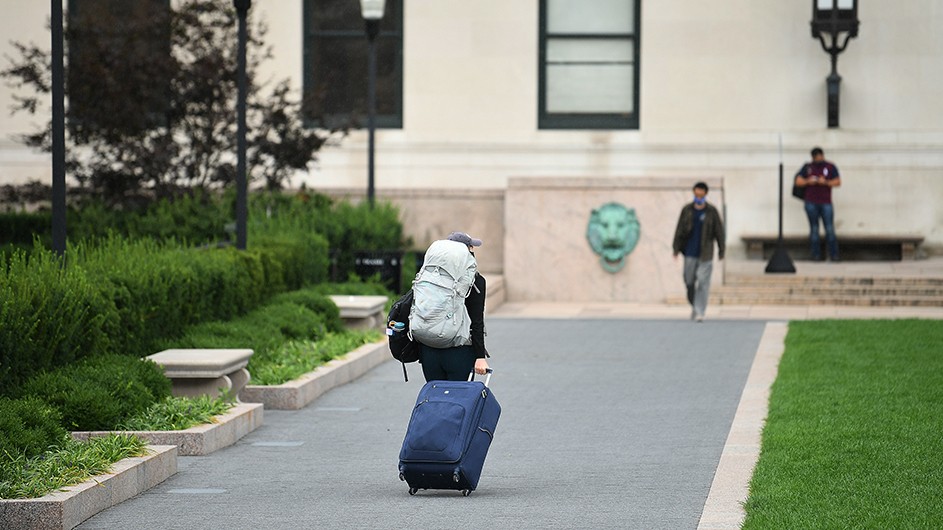 A student rolls a suitcase and backpack off Morningside campus. 
