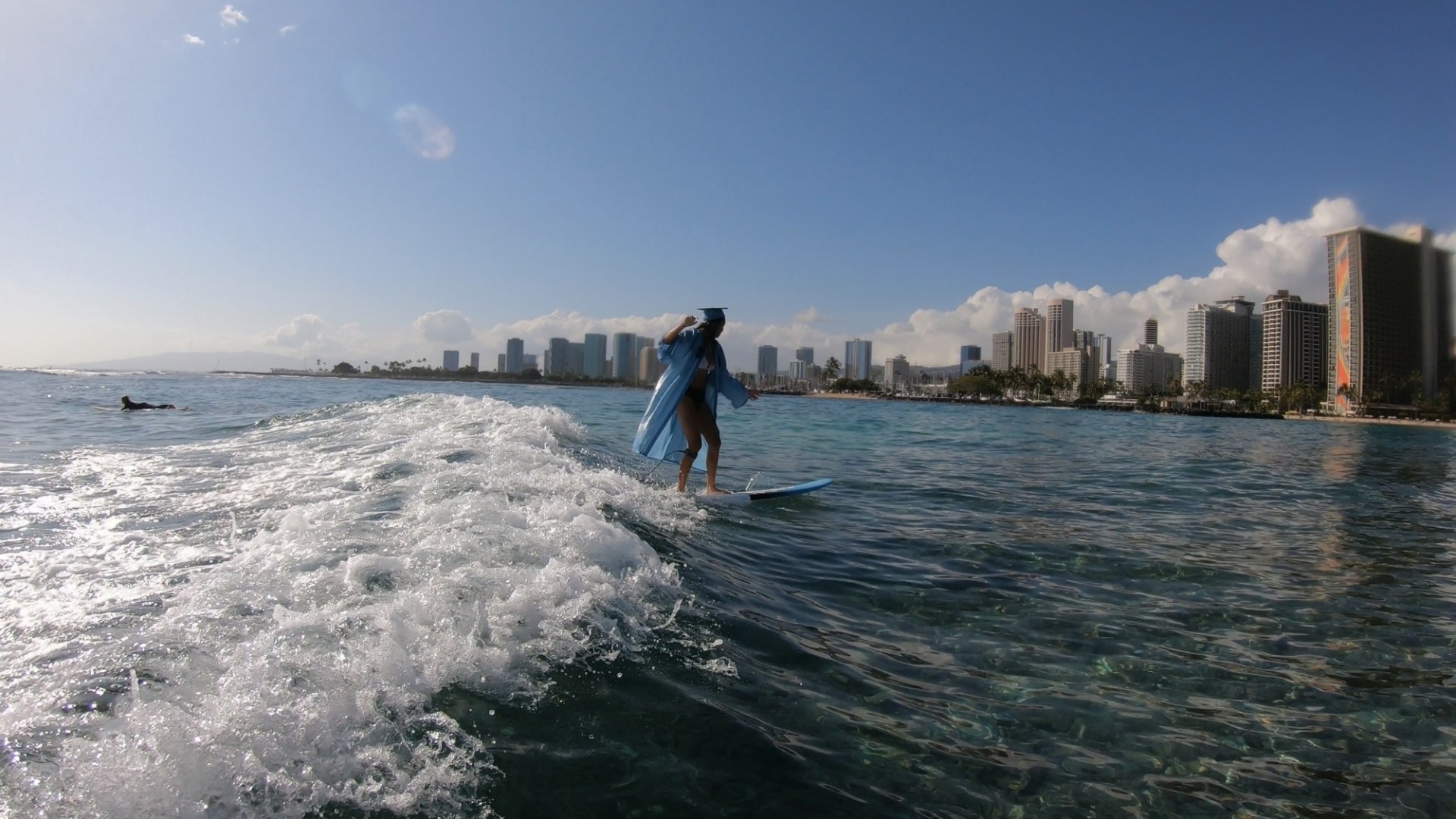 A Columbia grad in regalia surfs a wave in Honolulu, Hawaii. 