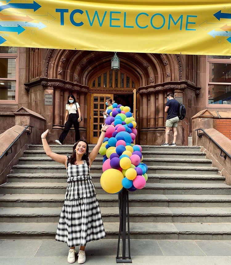 A student poses in front of the Teachers College Welcome sign and balloons. 